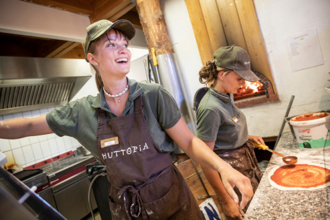Dos empleados alegres preparan pizza en la cocina de Camping Huttopia De Veluwe, Gelderland, Países Bajos.