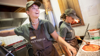 Zwei fröhliche Mitarbeiter bereiten Pizza zu in der Küche von Camping Huttopia De Veluwe, Gelderland.