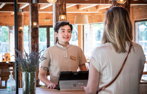 Recepcionista atendiendo a una huésped en la entrada de Camping Huttopia De Veluwe, Gelderland, Países Bajos.