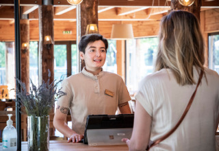 Receptionist verwelkomt gast aan de balie van Camping Huttopia De Veluwe, Gelderland, Nederland.