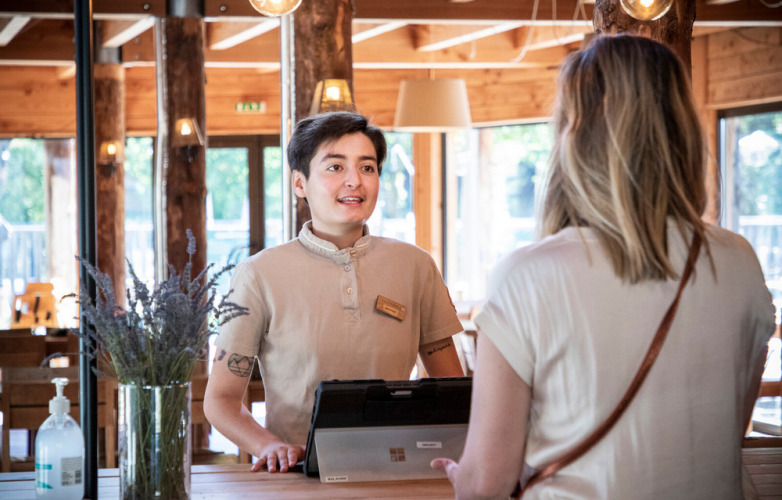 Réceptionniste accueillant une cliente à la réception du Camping Huttopia De Veluwe, en Guelderland, Pays-Bas.