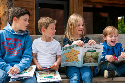 Niños sentados en un banco en Camping Huttopia De Veluwe, Gelderland, Países Bajos, leyendo libros de actividades.