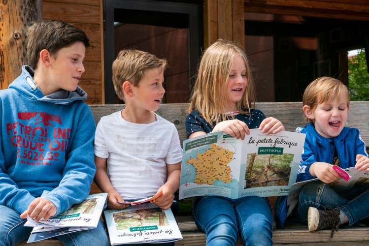 Des enfants assis sur un banc au Camping Huttopia De Veluwe, Gueldre, Pays-Bas, lisant des carnets d'activités.