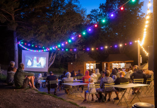 Buitenfilmavond met mensen die genieten van een film onder kleurrijke lampjes op Camping Huttopia De Veluwe.