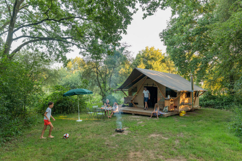Famiglia si gode il campeggio vicino a una tenda immersa nel verde a Huttopia De Veluwe, Gelderland.