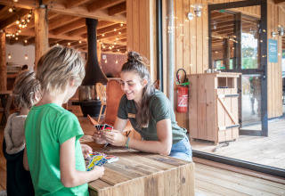 Kinderen spelen kaartspel met begeleidster in een houten chalet bij Camping Huttopia De Veluwe, Nederland.