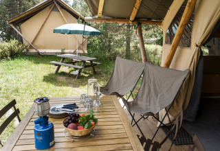 Mesa de madera al aire libre con cesta de frutas y hornillo junto a una tienda safari en Huttopia De Veluwe.