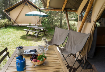 Mesa de madera al aire libre con cesta de frutas y hornillo junto a una tienda safari en Huttopia De Veluwe.