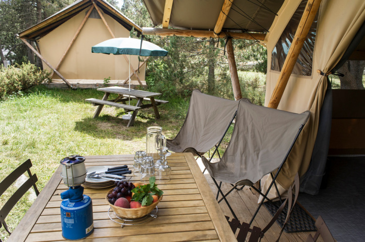Holztisch mit Stühlen, Obstkorb und Campingkocher auf einer Terrasse vor einem Safari-Zelt in den Niederlanden.