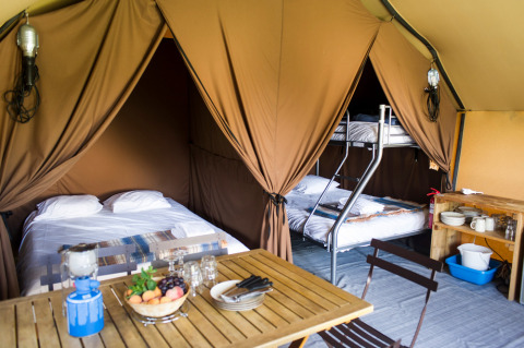 Interior de una tienda safari Canadienne Cosy en Camping Huttopia De Veluwe, Países Bajos, con camas y mesa.