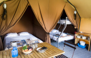 Interno di una tenda safari Canadienne Cosy al Camping Huttopia De Veluwe nei Paesi Bassi con letti e tavolo.