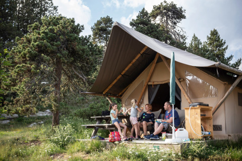 Una familia se relaja frente a una tienda safari en Camping Huttopia De Veluwe, rodeada de naturaleza en Holanda.
