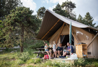 Una familia se relaja frente a una tienda safari en Camping Huttopia De Veluwe, rodeada de naturaleza en Holanda.