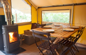 Interior de la tienda Canadienne Cosy en Camping Huttopia De Veluwe con mesa de madera y estufa.
