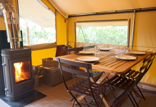 Innenraum eines Canadienne Cosy Safarizelts mit Esstisch, Holzofen und gelben Wänden auf Campingplatz.