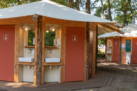 Servizi igienici da campeggio e lavabi moderni a Huttopia De Roos, parco vacanze in Overijssel, Paesi Bassi, immersi nel verde.
