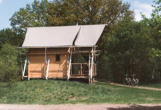 En hyggelig træhytte med telt-tag ved Huttopia De Roos feriepark i Overijssel, Holland, omgivet af natur.