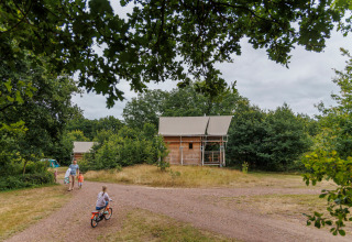 Familia paseando en bicicleta cerca de cabañas en Huttopia De Roos, un parque de vacaciones en Overijssel, Países Bajos.