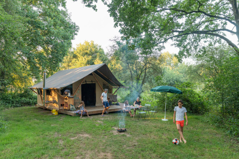 Gezin geniet voor een tent met kampvuur en voetbal bij Huttopia De Roos vakantiepark in Overijssel.
