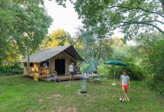 Famiglia si gode il tempo davanti a una tenda con falò e calcio a Huttopia De Roos, Overijssel, Paesi Bassi.