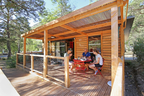 Cabaña de madera con terraza techada en el bosque, tres personas comiendo, Huttopia De Roos, Overijssel.