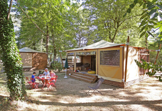 Familie nyder udendørs måltid foran glamping-hytte omgivet af træer på Huttopia De Roos, Overijssel.