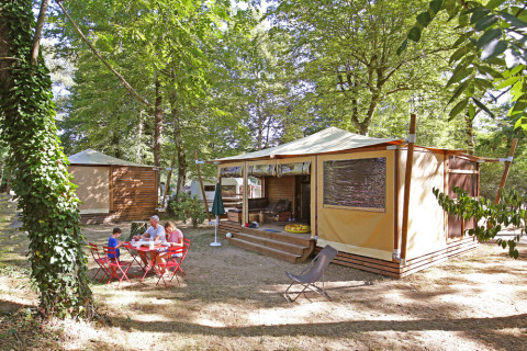 Family enjoys an outdoor meal by a glamping tent in the woods at Huttopia De Roos holiday park, Overijssel.