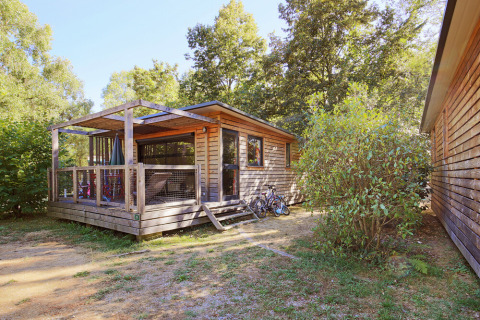 Wooden cabin with a porch and bicycles outside, set among trees at Huttopia De Roos, Overijssel, Netherlands.