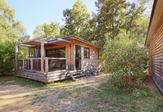 Holzhütte mit Veranda und Fahrrädern davor, umgeben von Bäumen im Huttopia De Roos, Overijssel, Niederlande.