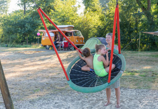 Familie hygger sig på en stor gynge på campingplads med VW-camper og telt i baggrunden i Overijssel.