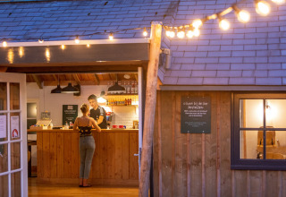 Aftenlys ved en udendørs bar på Huttopia De Roos feriepark i Overijssel, Holland, med to personer ved disken.