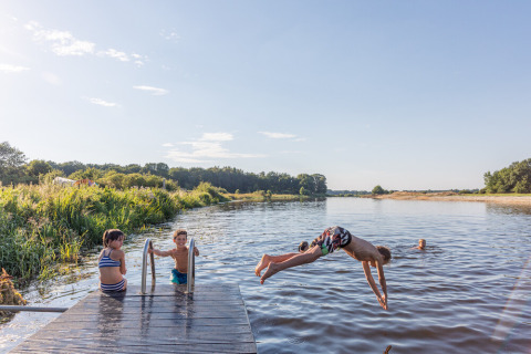 Niños juegan y nadan en un río junto a un muelle en Huttopia De Roos, un parque vacacional en Overijssel, Países Bajos.