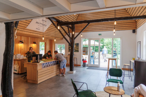 Receptionen på Huttopia De Roos feriepark i Overijssel, Nederlandene, med træinteriør og folk ved skranken.
