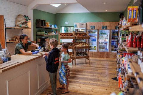 Dos niños compran en una acogedora tienda del parque vacacional Huttopia De Roos en Overijssel, Países Bajos.