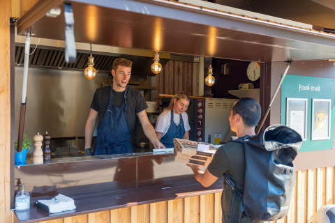 Een bezorger haalt pizza af bij een foodtruck op Huttopia De Roos vakantiedomein in Overijssel, Nederland.