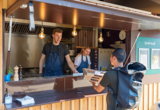 En leveringschauffør afhenter pizza fra et udendørs madbod på Huttopia De Roos i Overijssel, Holland.