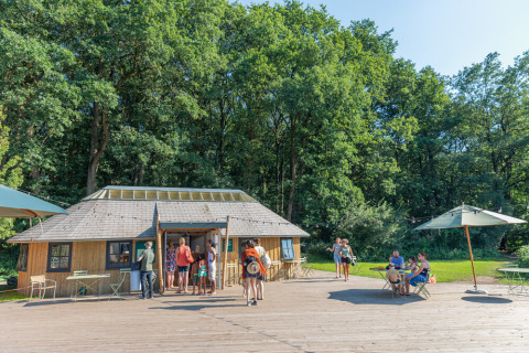 Parque vacacional Huttopia De Roos en Overijssel, Países Bajos, con visitantes cerca de una cabaña de madera.