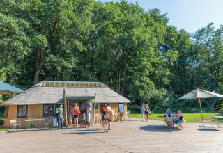 Feriepark Huttopia De Roos i Overijssel med gæster foran en træhytte og folk, der nyder solen udendørs.