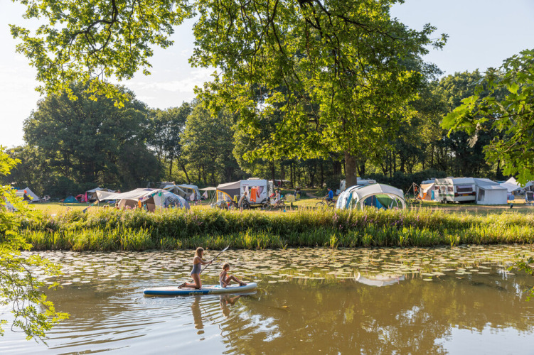 Twee kinderen peddelen op de rivier bij Huttopia De Roos tussen tenten en bomen in Overijssel, Nederland.