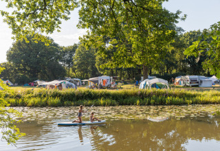 Two children paddle on a river at Huttopia De Roos holiday park with tents and trees in Overijssel, Netherlands.