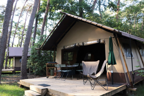 Tenda safari Classic Wood Tent nella foresta con terrazza in legno, tavolo, sedie e ombrellone.