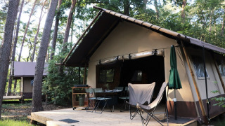Tenda safari Classic Wood Tent nella foresta con terrazza in legno, tavolo, sedie e ombrellone.