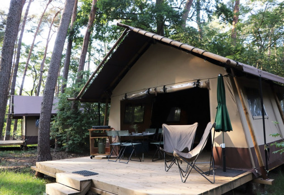 Classic Wood Tent safari tent set in the forest with outdoor deck, table, chairs, and umbrella.
