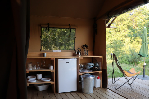 Area cucina in una tenda safari con frigo, stoviglie e vista sulla natura a Huttopia De Roos, Paesi Bassi.