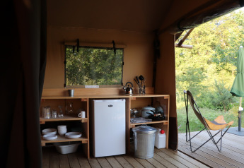 Area cucina in una tenda safari con frigo, stoviglie e vista sulla natura a Huttopia De Roos, Paesi Bassi.