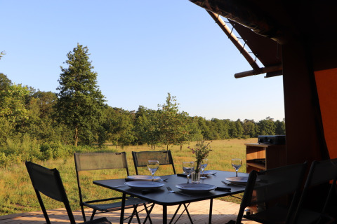 Mesa de comedor al aire libre en la tienda safari Classic Wood Tent de Huttopia De Roos, Países Bajos, con vista al bosque.