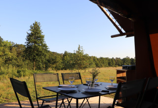 Mesa de comedor al aire libre en la tienda safari Classic Wood Tent de Huttopia De Roos, Países Bajos, con vista al bosque.