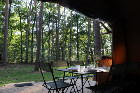Area pranzo all’aperto su terrazza in legno al Classic Wood Tent di Huttopia De Roos, Paesi Bassi, vista foresta.