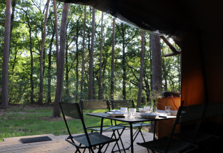 Essbereich auf einer Holzterrasse im Wald bei einem Classic Wood Tent auf Huttopia De Roos, Niederlande.