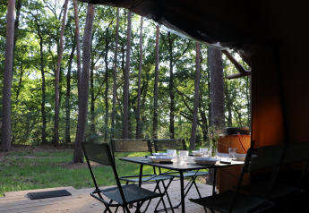 Area pranzo all’aperto su terrazza in legno al Classic Wood Tent di Huttopia De Roos, Paesi Bassi, vista foresta.